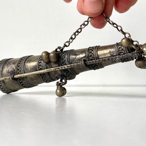 Könnte beinhalten: Ein verzierter, dekorativer, hängender Metallbehälter in Silberton mit einer Kette und Glöckchen.