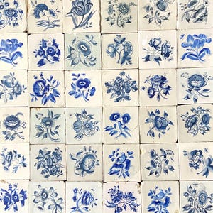 May include: A collection of square ceramic tiles with hand-painted floral designs in shades of blue on a white background. The tiles feature various flower and leaf patterns, creating a vintage aesthetic. The tiles are arranged in a grid.