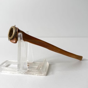 May include: A long, slender, brown, tapered object with a smooth, polished finish. At the wider end, there is a circular, metallic, brass-colored rim or fitting attached to the top, creating a distinct contrast with the brown material.