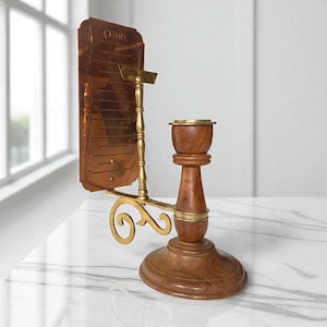 Puede incluir: Un candelabro antiguo de madera y latón con una placa de color cobre. La placa tiene la palabra "CUNO" en la parte superior. El candelabro tiene una base redonda y un brazo decorativo de latón curvado.