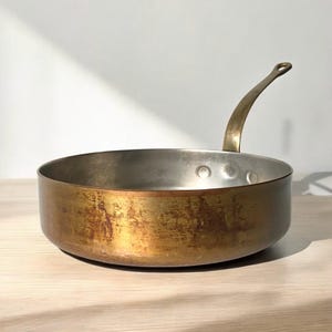 May include: A vintage copper saucepan with a long handle. The saucepan has a worn, aged patina and is suitable for cooking on a stovetop.
