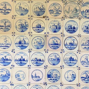May include: A collection of square ceramic tiles with hand-painted blue and white illustrations. Each tile features a circular scene of Dutch landscapes, including windmills, houses, and figures. The tiles are arranged in a grid pattern.