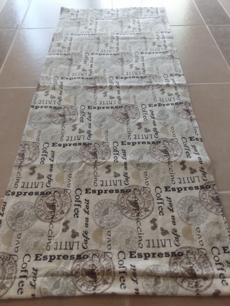 Puede incluir: Tela blanca con un patr&oacute;n repetido de ilustraciones marrones con tem&aacute;tica de caf&eacute;. Las ilustraciones incluyen granos de caf&eacute;, tazas de caf&eacute; y las palabras "Espresso", "Latte", "Cappuccino", "Coffee" y "Cafe au Lait".