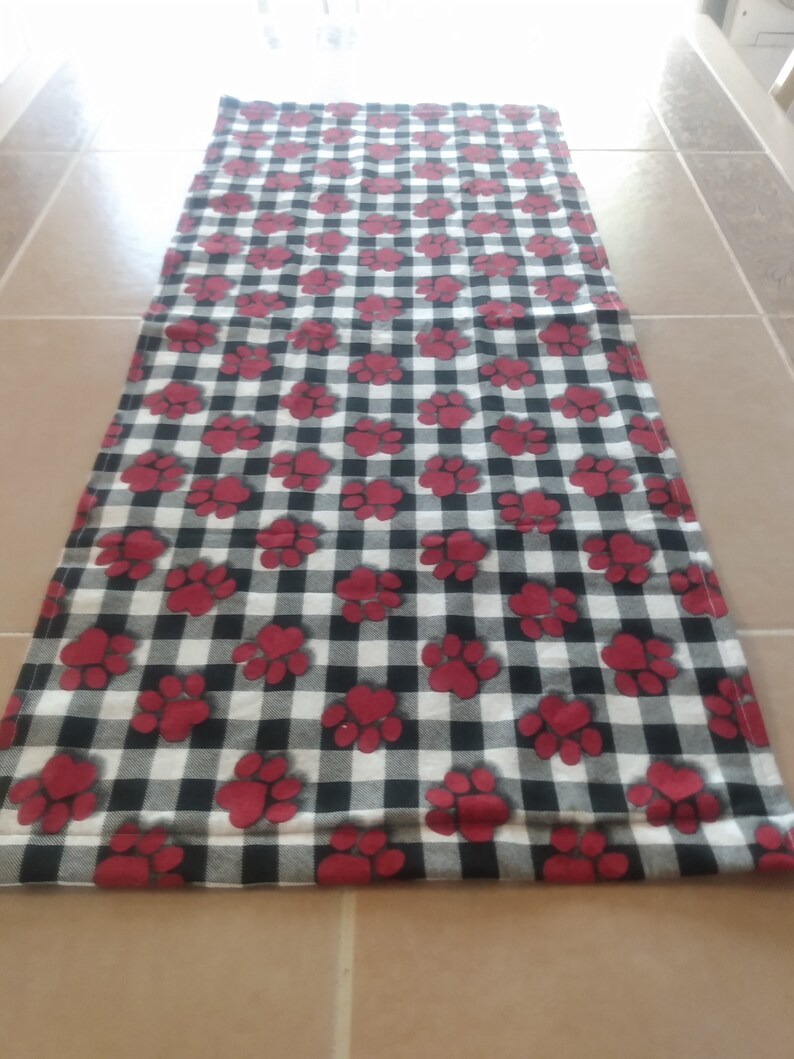 K&ouml;nnte beinhalten: Schwarzer und wei&szlig;er karierter L&auml;ufer mit roten Pfotenabdr&uuml;cken.