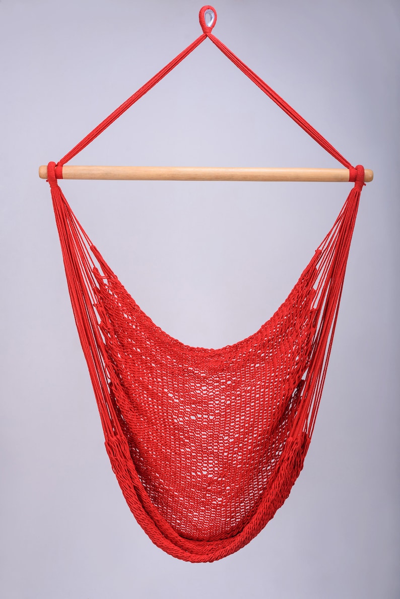 Puede incluir: Una silla hamaca roja con una barra de extensi&oacute;n de madera. La hamaca est&aacute; hecha de cuerda tejida y est&aacute; colgada de un gancho de techo.