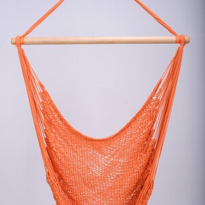 Puede incluir: Una silla hamaca naranja colgando de una barra de madera. La hamaca est&aacute; hecha de un material de cuerda trenzada.
