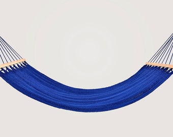 May include: A blue hammock with wooden spreader bars. The hammock is made of woven cotton rope and is hanging from two ropes.
