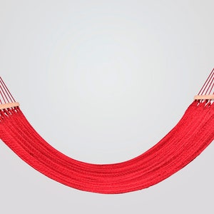 May include: A red hammock with wooden spreader bars. The hammock is made of woven rope and is hanging from two points.