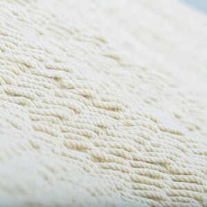 May include: Close-up of a white woven macrame wall hanging with a textured pattern.