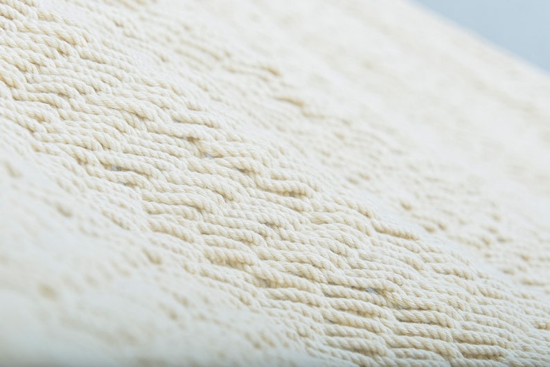 May include: Close-up of a white woven macrame wall hanging with a textured pattern.