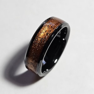 以下が含まれることがあります： 銅色の素材と金色のフレークが入った黒い指輪。 リングは研磨仕上げで、シンプルでエレガントなデザインです。 リングはおそらくセラミックまたは同様の素材で作られています。