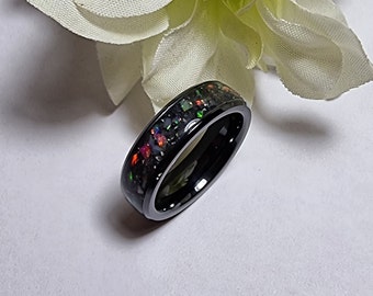 May include: A black ceramic ring with a band of iridescent opal inlay. The ring is a simple design with a smooth, polished finish.