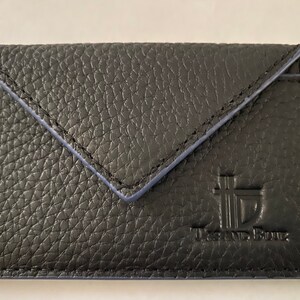 Op de afbeelding: Zwarte leren kaarthouder met een blauwe gestikte envelopklep en de gegraveerde tekst "The Brand Box".