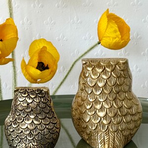 May include: Two gold metal owl figurines with a scaly texture. The owls are facing forward with their wings spread out.