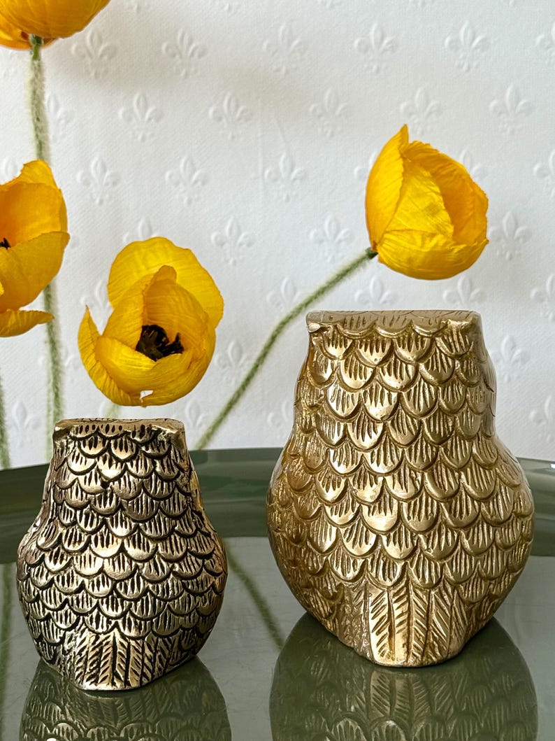 May include: Two gold metal owl figurines with a scaly texture. The owls are facing forward with their wings spread out.