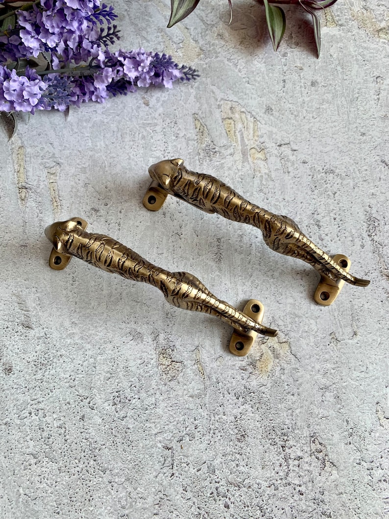 May include: Two brass door handles shaped like a crouching tiger. The handles are detailed with a tiger stripe pattern and have a gold finish.