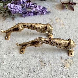 May include: Two gold-toned tiger door handles with detailed features. The handles are made of metal and have a realistic tiger design.