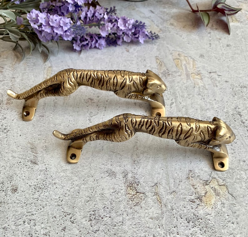 May include: Two gold-toned tiger door handles with detailed features. The handles are made of metal and have a realistic tiger design.
