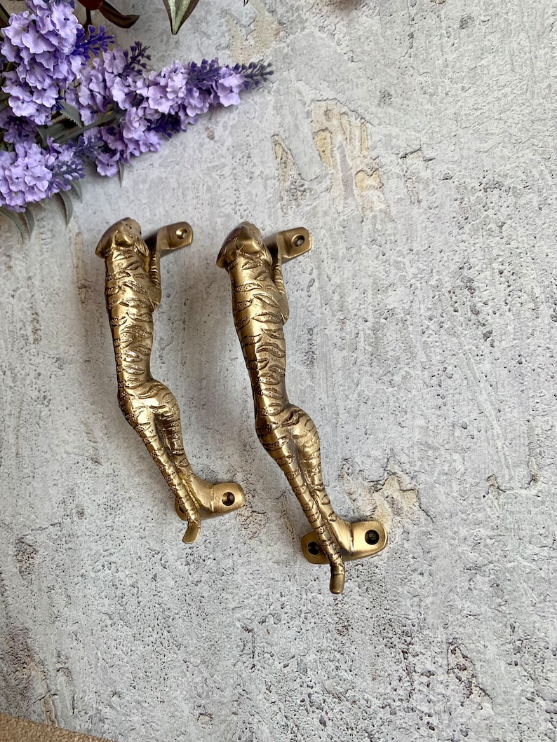 May include: A pair of gold-toned metal door handles shaped like a cheetah. The handles are detailed with a cheetah print pattern.