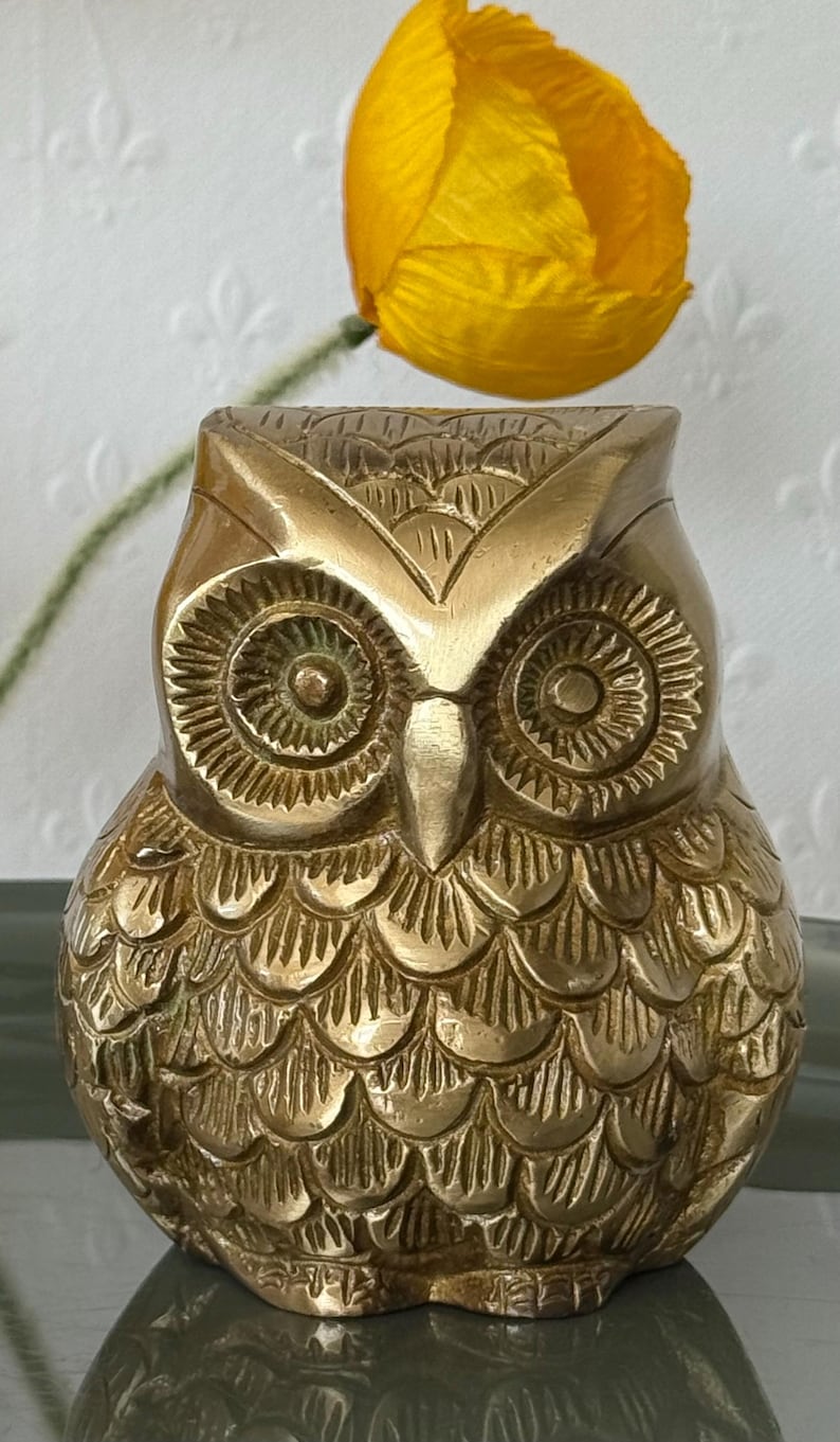 May include: A gold-colored brass owl figurine with detailed carvings. The owl has large, round eyes and a textured body.