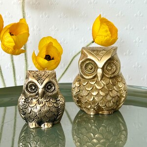 May include: Two gold owl figurines with detailed feather patterns. The larger owl is slightly taller than the smaller owl.