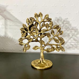 May include: A gold metal tree sculpture with intricate branches and leaves. The tree is on a dark brown surface.