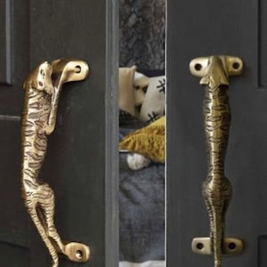 May include: Two gold-toned door handles shaped like a tiger. The handles are mounted on a dark gray door.