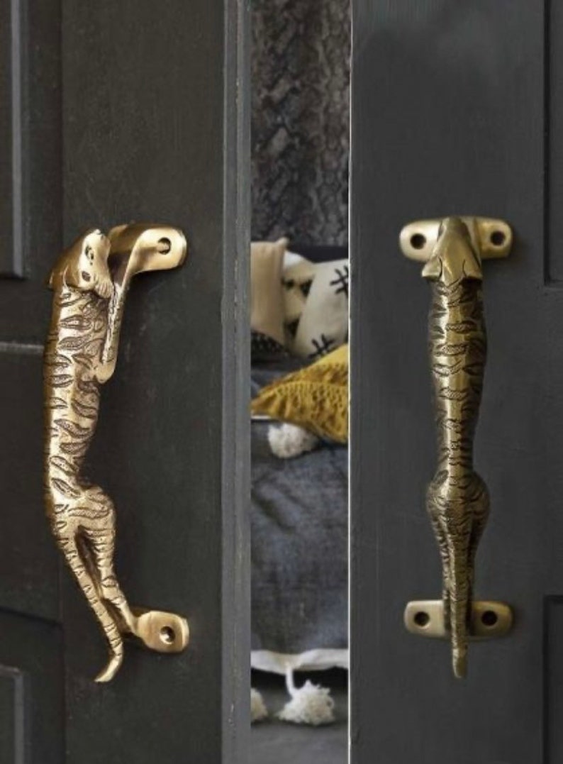 May include: Two gold-toned door handles shaped like a tiger. The handles are mounted on a dark gray door.