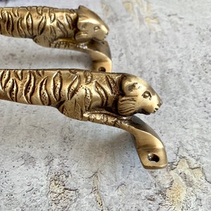 May include: A pair of brass door handles shaped like tiger heads. The handles are detailed with tiger stripes and have a polished finish.