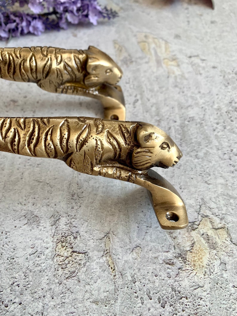 May include: A pair of brass door handles shaped like tiger heads. The handles are detailed with tiger stripes and have a polished finish.