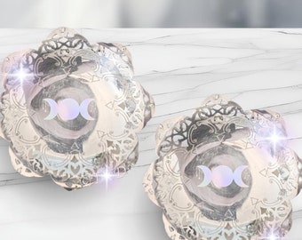 May include: Two silver metal bowls with a decorative, lacy design. Each bowl features a triple moon symbol in the center.