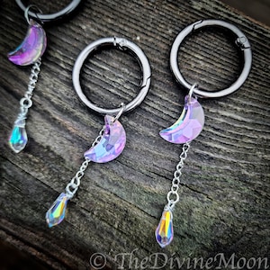 May include: Three silver keychains with iridescent purple crescent moon charms and teardrop crystals hanging from them.