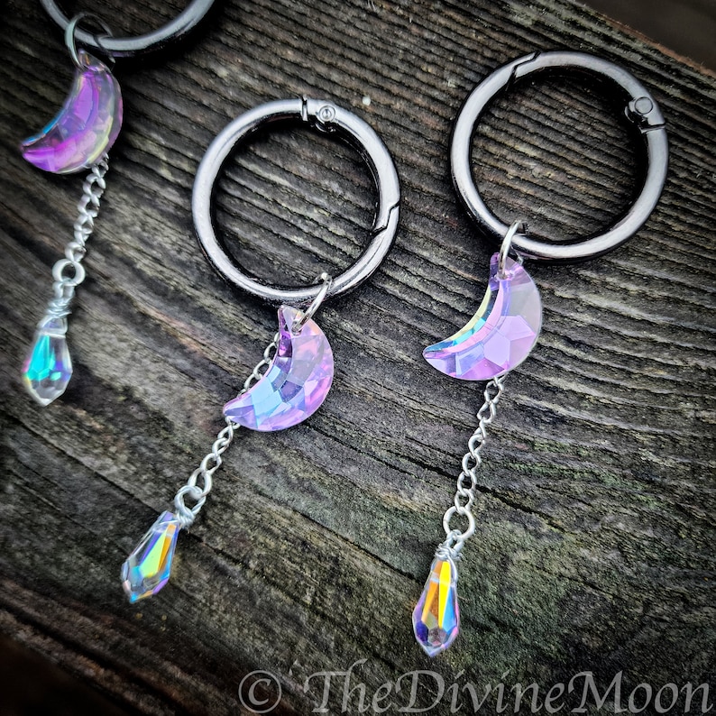 May include: Three silver keychains with iridescent purple crescent moon charms and teardrop crystals hanging from them.