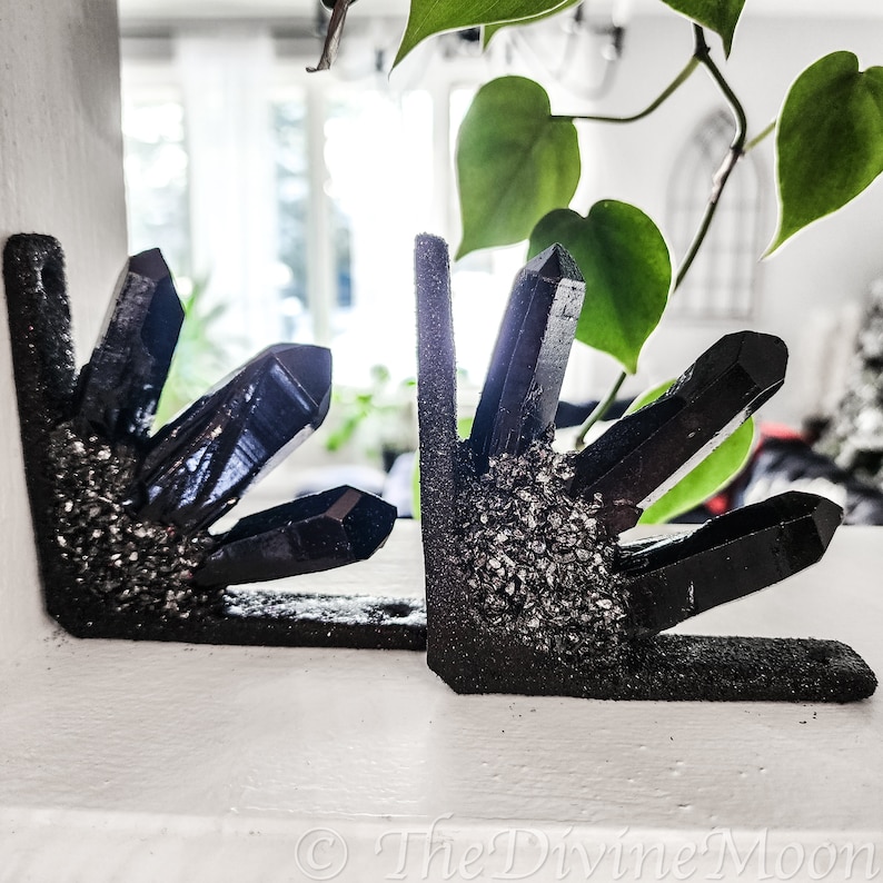 May include: Two black crystal bookends with silver glitter accents. The bookends are shaped like clusters of crystals and are displayed on a white surface.