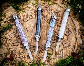 May include: Four cylindrical glass wands filled with small gemstone chips, including purple amethyst, black obsidian, multicolored fluorite, and clear quartz. Each wand features silver-toned metal caps and a pointed crystal tip at the base.