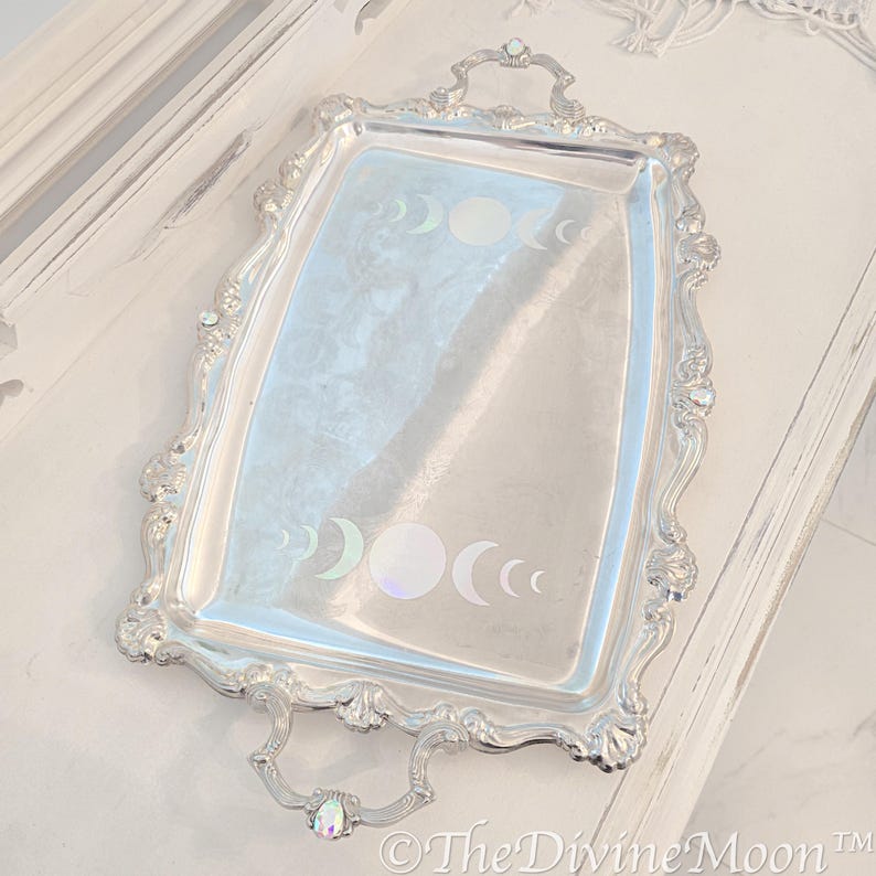 May include: A silver serving tray with ornate edges and two handles. The tray features a design of iridescent moon phases.