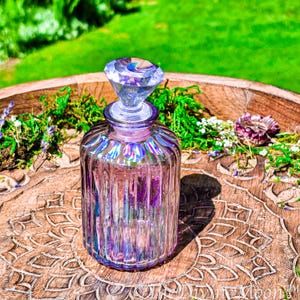 Puede incluir: Una botella de vidrio iridiscente morado con acanalado vertical y un tap&oacute;n facetado en forma de diamante. El cuello de la botella est&aacute; decorado con una serie de peque&ntilde;as pegatinas hologr&aacute;ficas circulares de fases lunares.