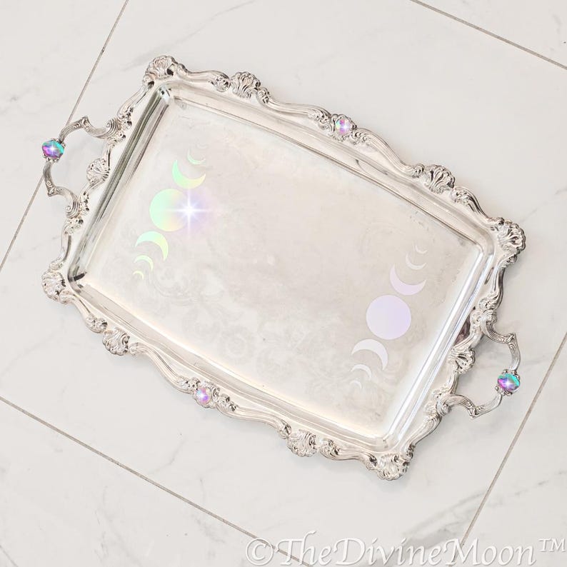 May include: A silver serving tray with ornate edges and iridescent moon phases decals. The tray has two handles with iridescent gemstone accents.