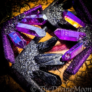 May include: A close-up of a pair of black and purple crystal earrings. The crystals are iridescent and have a sparkly finish. The earrings are on a wooden surface.