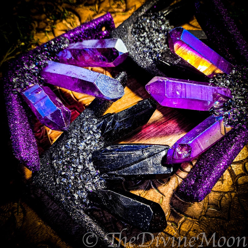 May include: A close-up of a pair of black and purple crystal earrings. The crystals are iridescent and have a sparkly finish. The earrings are on a wooden surface.