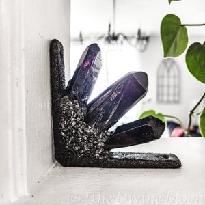 May include: A black crystal corner shelf with a glittery black finish. The shelf is shaped like a cluster of crystals and has a sharp, pointed design. The shelf is a decorative home decor item.