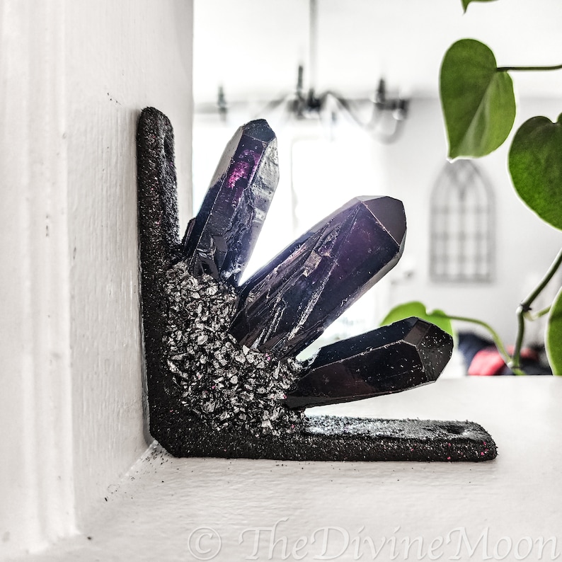 May include: A black crystal corner shelf with a glittery black finish. The shelf is shaped like a cluster of crystals and has a sharp, pointed design. The shelf is a decorative home decor item.