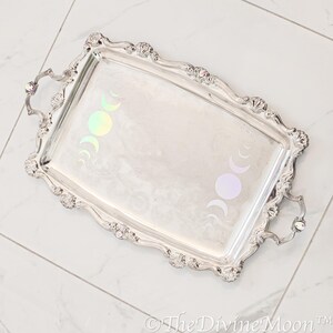 May include: A silver serving tray with ornate edges and two handles. The tray features a design of iridescent moon phases.