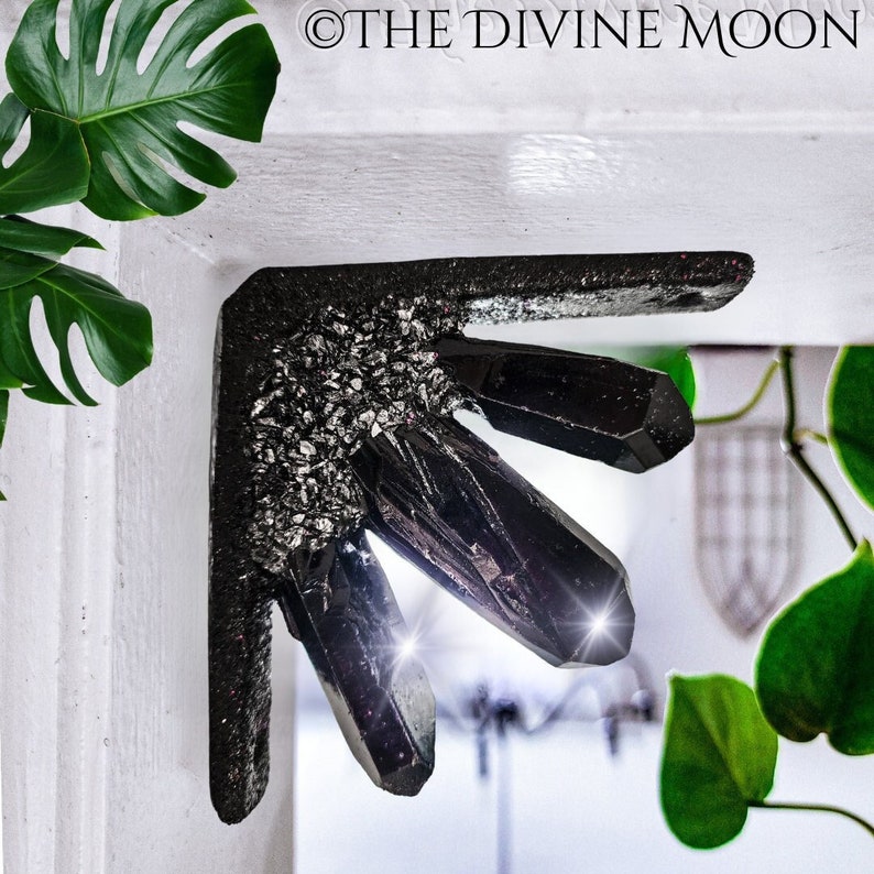 May include: A black crystal corner shelf with a silver glitter finish. The shelf is shaped like a cluster of crystals and is mounted on a white wall.