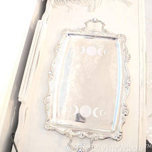 May include: A silver serving tray with a decorative, ornate border. The tray features a design of three crescent moons and a full moon in the centre.