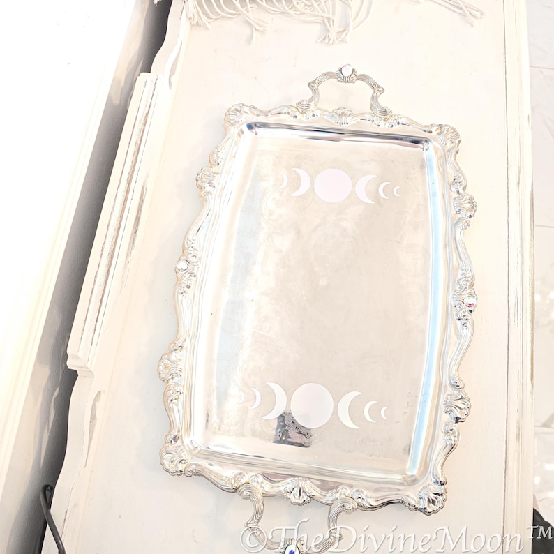 May include: A silver serving tray with a decorative, ornate border. The tray features a design of three crescent moons and a full moon in the centre.