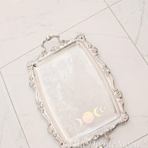 May include: A silver serving tray with an ornate design and a handle. The tray features a moon phase design in iridescent colours.