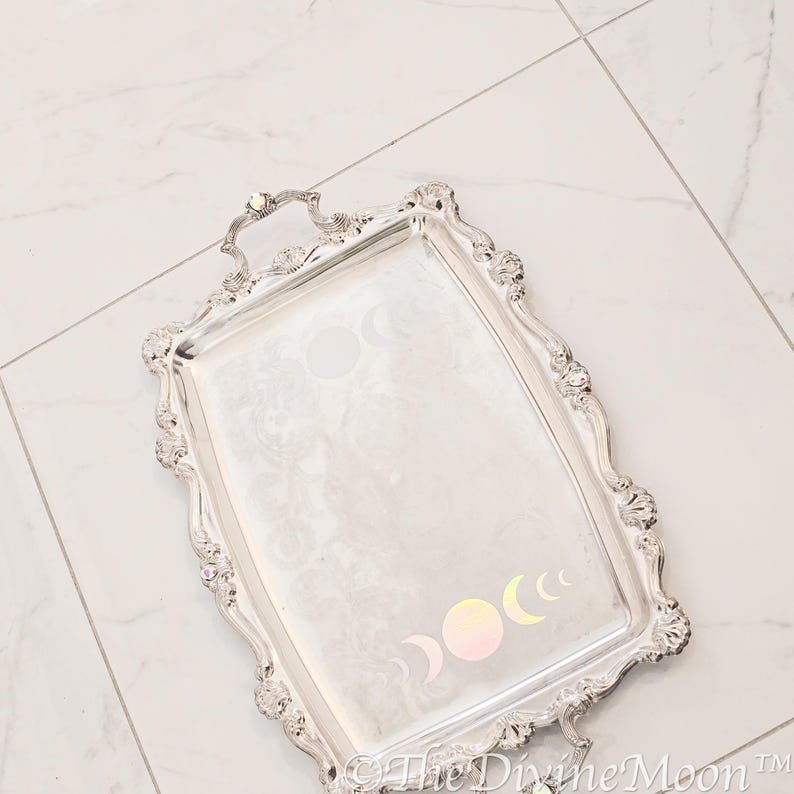 May include: A silver serving tray with an ornate design and a handle. The tray features a moon phase design in iridescent colours.