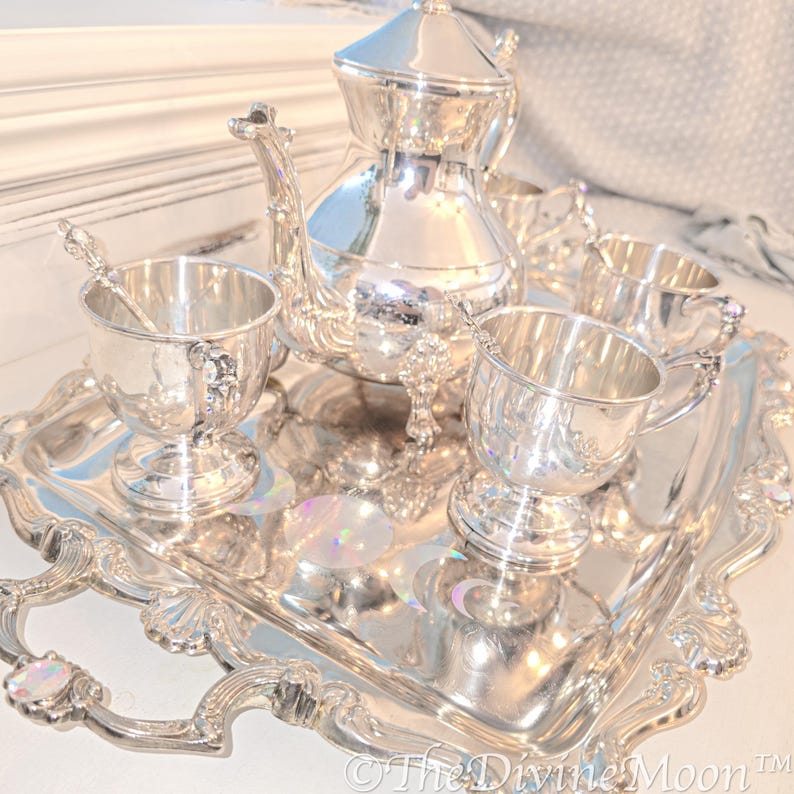 May include: A silver tea set with a teapot, creamer, sugar bowl, and four cups on a silver tray with ornate detailing.