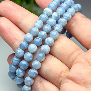 May include: A multi-strand bracelet composed of smooth, round, light blue beads with subtle white marbled patterns. The beads have a polished, glossy finish and are strung together in a continuous loop, showcasing a consistent spherical shape.